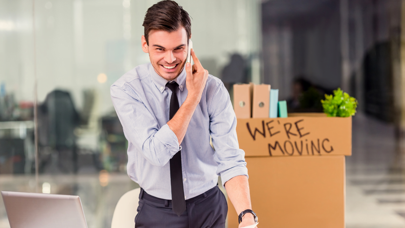 Picture of a box with we're moving on it and man with a phone to his ear